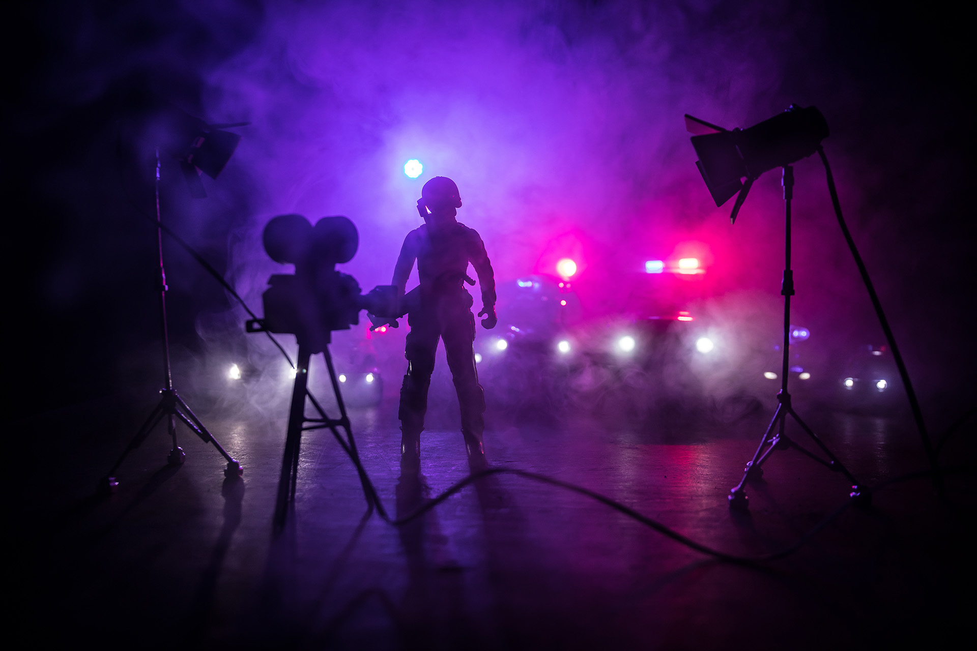 Action movie concept. Police cars and miniature movie set on dark toned background with fog. Police car chasing a car at night. Scene of crime accident.